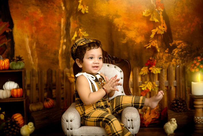 A child in a patterned yellow clothes sitting on a chair with a candle burning nearby him during his photoshoot Captured by Meghna Rathore Delhi NCR, Haryana best maternity and child photographer.