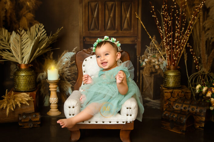 The child wears a flower crown and teal fabric, surrounded by ornate decor sitting on a white chair captured by Meghna Rathore Delhi NCR, Haryana best maternity and child photographer.