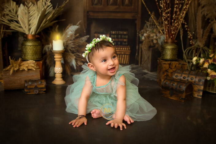 Smiling like a little angle a one year baby girl wearing floral tiara in an rustic antique surrounding captured by Meghna Rathore Delhi NCR, Haryana best maternity and child photographer.