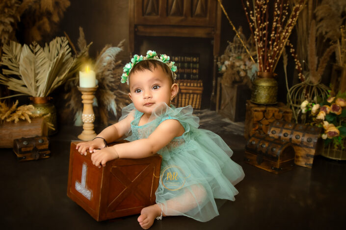 A baby girl in teal green dress playing with a wooden box during her pre birthday photoshoot by Meghna Rathore