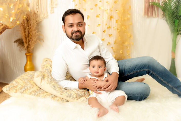 Sitting on fury bed a father holding his baby boy surrounding by aesthetic beauty in golden theme captured by Meghna Rathore, Delhi NCR's best maternity and child photographer.