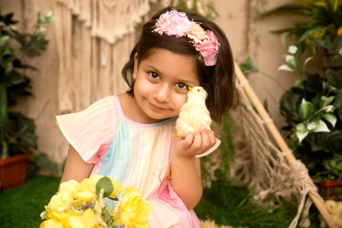 A girl holding a little bird close to her chick wearing a lite pink and yellow dress holding yellow flowers captured by Meghna Rathore best maternal and child photographer in Delhi, NCR.