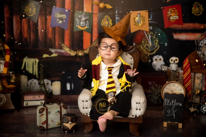 A charming Harry Potter-themed setting with a child dressed as a young wizard. The child, whose face is obscured for privacy, is seated on an ornate by the best maternity and child photographer Meghna Rathore Delhi NCR, Haryana.