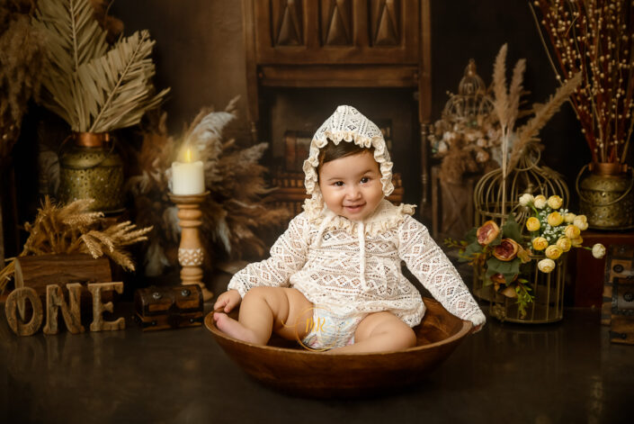 A cute little child sitting in a wooden bowl giving a simile look with an interesting eye expression celebrating first birthday captured by the best maternity and child photographer Meghna Rathore Delhi NCR, Haryana.