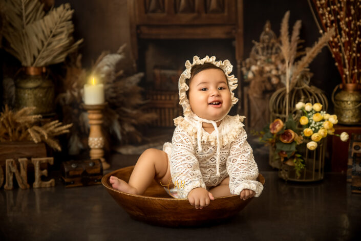 This image captures a child in vintage attire, seated in a wooden bowl amidst a rustic setting, evoking a sense of nostalgia and timeless beauty captured by the best maternity and child photographer Meghna Rathore Delhi NCR, Haryana.