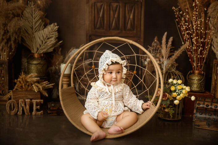 A baby sits in a circular frame, surrounded by vintage decorations, celebrating a first birthday, evoking warmth and nostalgia. Captured by Delhi NCR best child photographer Meghna Rathore.