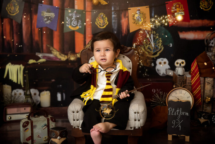 A child in Harry Potter attire and sitting in a place with a Harry Potter theme surrounding, giving a very thinkable look with the magic wand captured by the best maternity and child photographer Meghna Rathore Delhi NCR, Haryana.