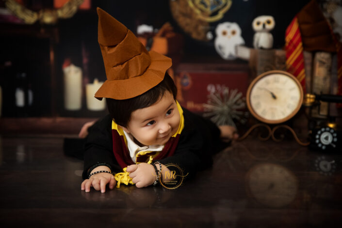 A child in wizard attire sits amidst magical paraphernalia, evoking a whimsical, Harry Potter-like atmosphere, showcasing innocence intertwined with fantastical elements captured by the best maternity and child photographer Meghna Rathore Delhi NCR, Haryana.