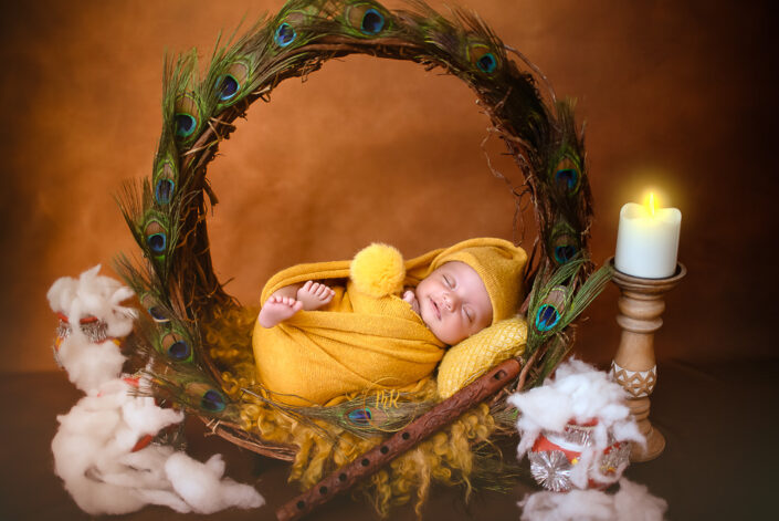 A sleeping baby wrapped in yellow, surrounded by peacock feathers, cotton, and a lit candle creates a serene atmosphere captured by Meghna the best photographer in Delhi NCR