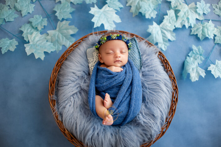 This captivating image portrays a baby wrapped in blue cloth, nestled on a cloud-shaped pillow. The serene scene exudes innocence and tranquility by Meghna Rathore Delhi NCR best child and maternity photographer