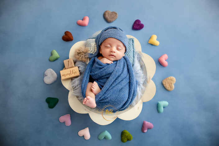 one month baby girly surrounded by hearts in a bluish theme surrounding captured by meghna rathore Delhi NCR best child and maternity photograapher.