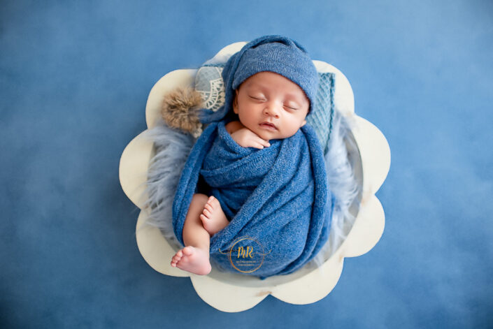 A baby wrapped in blue cloth lies on a cloud-shaped pillow, showcasing the innocence and peacefulness of early childhood by meghna rathore Delhi NCR best maternity and child photographer