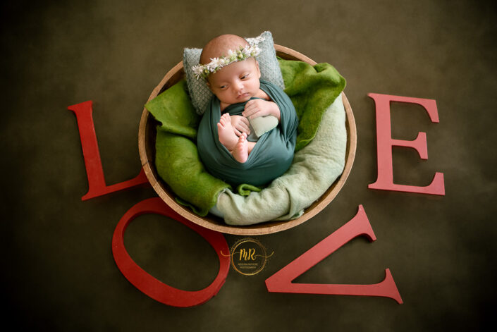A baby girl in wooden bowl covered with green cloth and surrounded by letter Love captured by Meghna Rathore best maternity and child photographer Delhi NCR