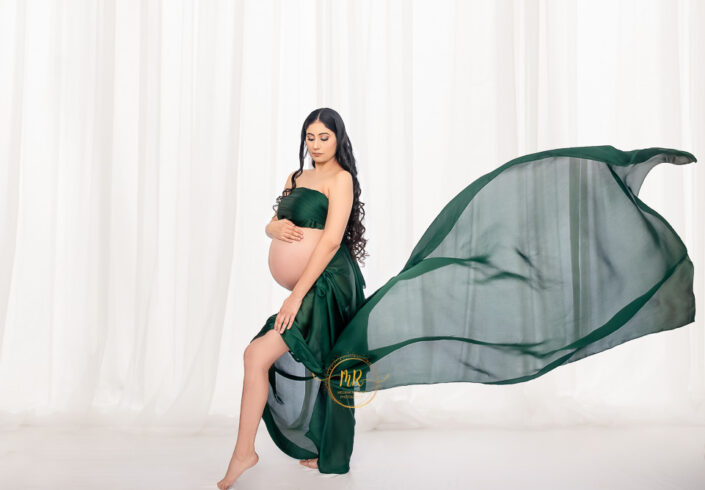 Meghna Rathore photography, Delhi NCR, Haryana, maternity photoshoot by the best photographer, pregnant women wearing a lower cut green stain maternity gown blown by slow wind like her life.