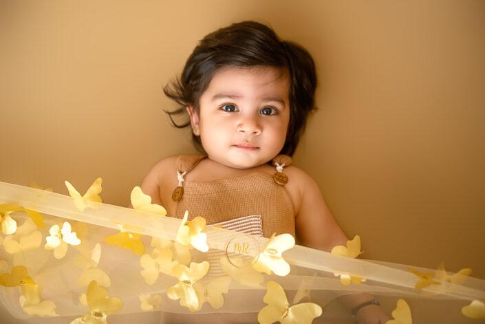 A child, face hidden, stands amidst a flurry of yellow butterflies, creating an artistic, whimsical scene that evokes fantasy and sparks creativity by the best maternity and Pre-Birthday child photographer Meghna Rathore Delhi NCR, Haryana.