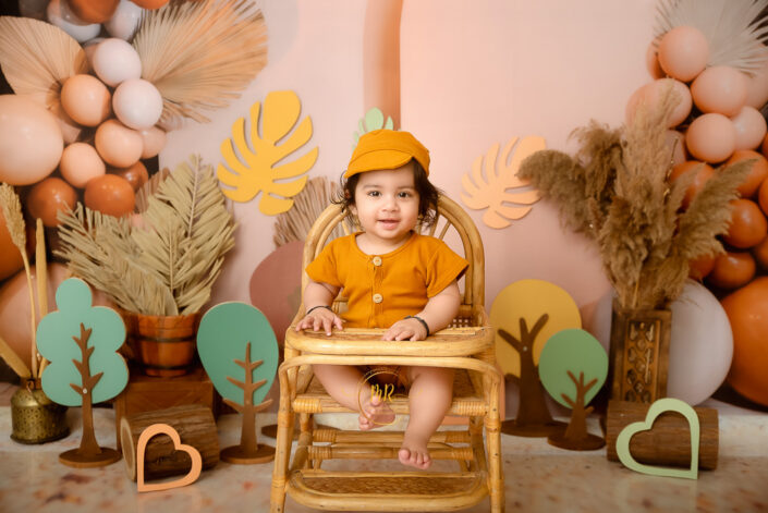A child sits in a wooden chair, surrounded by whimsical wooden hearts and trees, creating a warm, playful, and cozy atmosphere of innocence and wonder during pre Birthday Photoshoot by Meghana Rathore Delhi NCR best maternity and child photographer