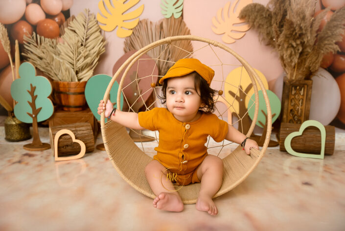 A child sits in a circular chair, surrounded by whimsical wooden hearts and trees, creating a warm, playful, and cozy atmosphere of innocence and wonder by the best maternity and Pre-Birthday child photographer Meghna Rathore Delhi NCR, Haryana.