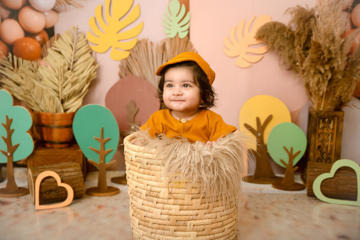 A child sits in a basket amidst a colorful, whimsical setting, capturing the innocence and wonder of childhood in a creatively decorated environment by the best maternity and Pre-Birthday child photographer Meghna Rathore Delhi NCR, Haryana.