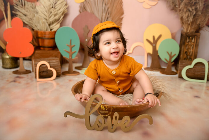 A little baby in a wooden bowl having some playful moments during pre Birthday Photoshoot by Delhi NCR best maternity and child photographer.