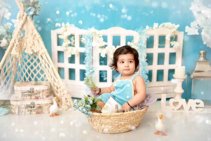 The child is surrounded by whimsical decorations, including a white wooden fence structure adorned with flowers and the word ‘love’, and a small tent resembling a teepee by the best maternity and Pre-Birthday child photographer Meghna Rathore Delhi NCR, Haryana.