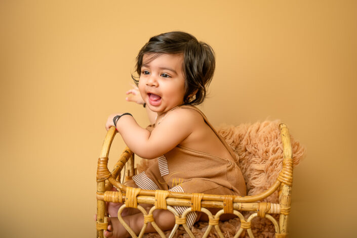 A child sits in a woven basket, evoking warmth and innocence against a harmonious monochromatic background by the best maternity and Pre-Birthday child photographer Meghna Rathore Delhi NCR, Haryana.