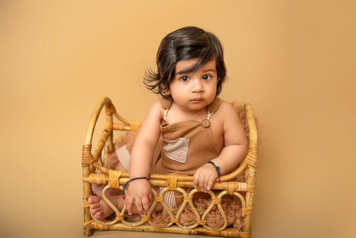 A baby child sitting in a wooden palki during her pre-birthday photoshoot by the best maternity and Pre-Birthday child photographer Meghna Rathore Delhi NCR, Haryana.