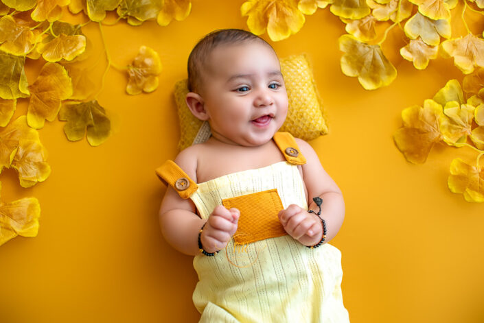 Smiling baby in a yellow flowery background captured by Meghna Rathore, Delhi NCR's best maternity and child photographer.