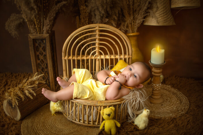 A boy is liking his figures lying in a wooden bed surrounded by chicks and a small Mr. bean teady captured by Meghna Rathore, Delhi NCR's best maternity and child photographer.