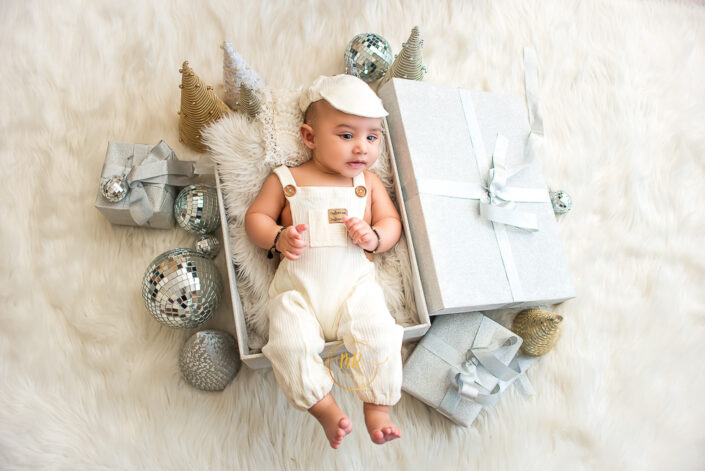 A child in white dress and a cap in a gift box surrounded by gifts and party accessories captured by Meghna Rathore, Delhi NCR's best maternity and child photographer.