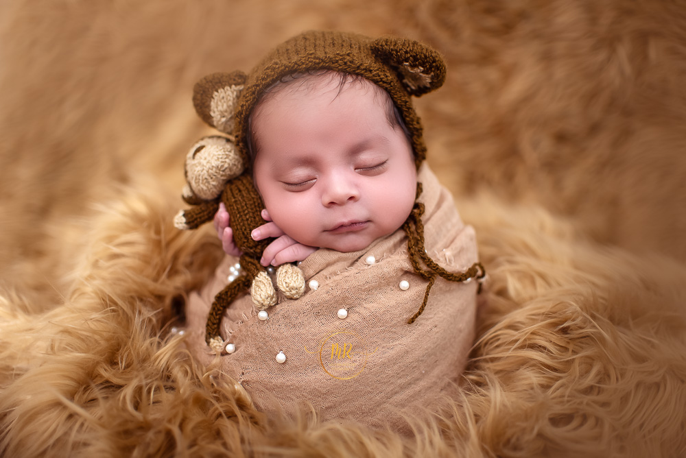 A newborn baby boy wrapped in a brown blanket and holding a monkey doll captured by Delhi NCR's best maternal photographer Meghna Rathore.