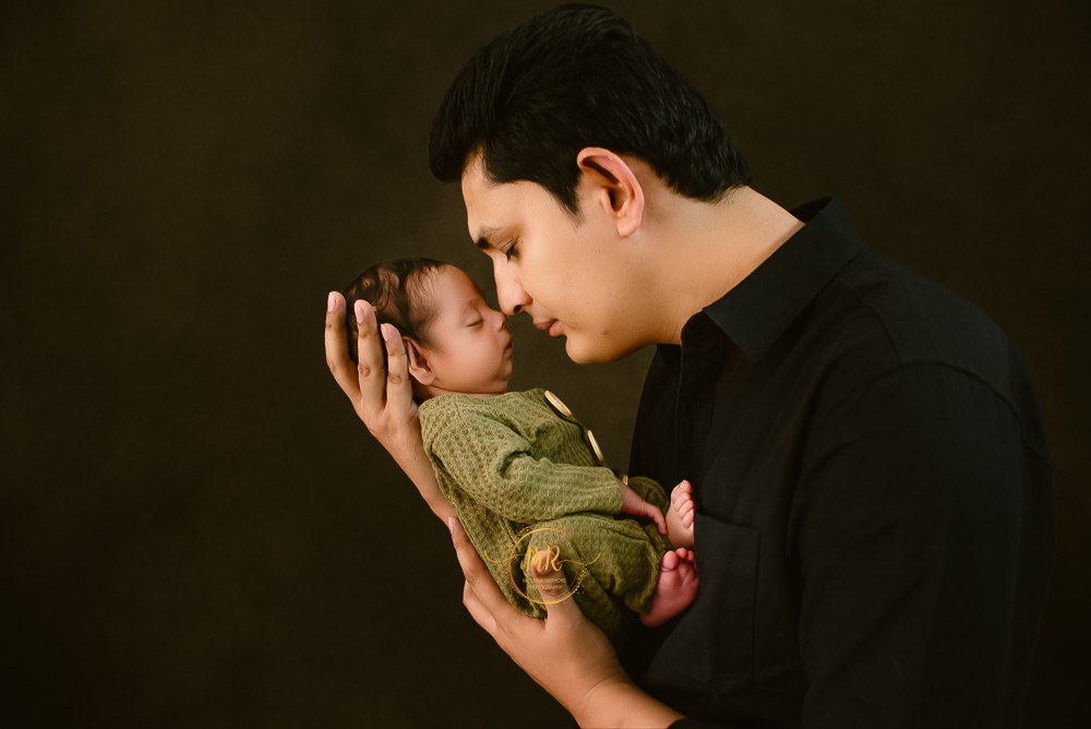 A father holding his newborn baby, displaying a heartwarming moment of parental care and affection captured by Delhi NCR's best maternal photographer Meghna Rathore.